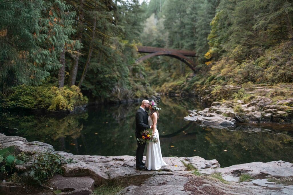 a bride and groom kiss with a creek and bridge behind them in portland oregon 