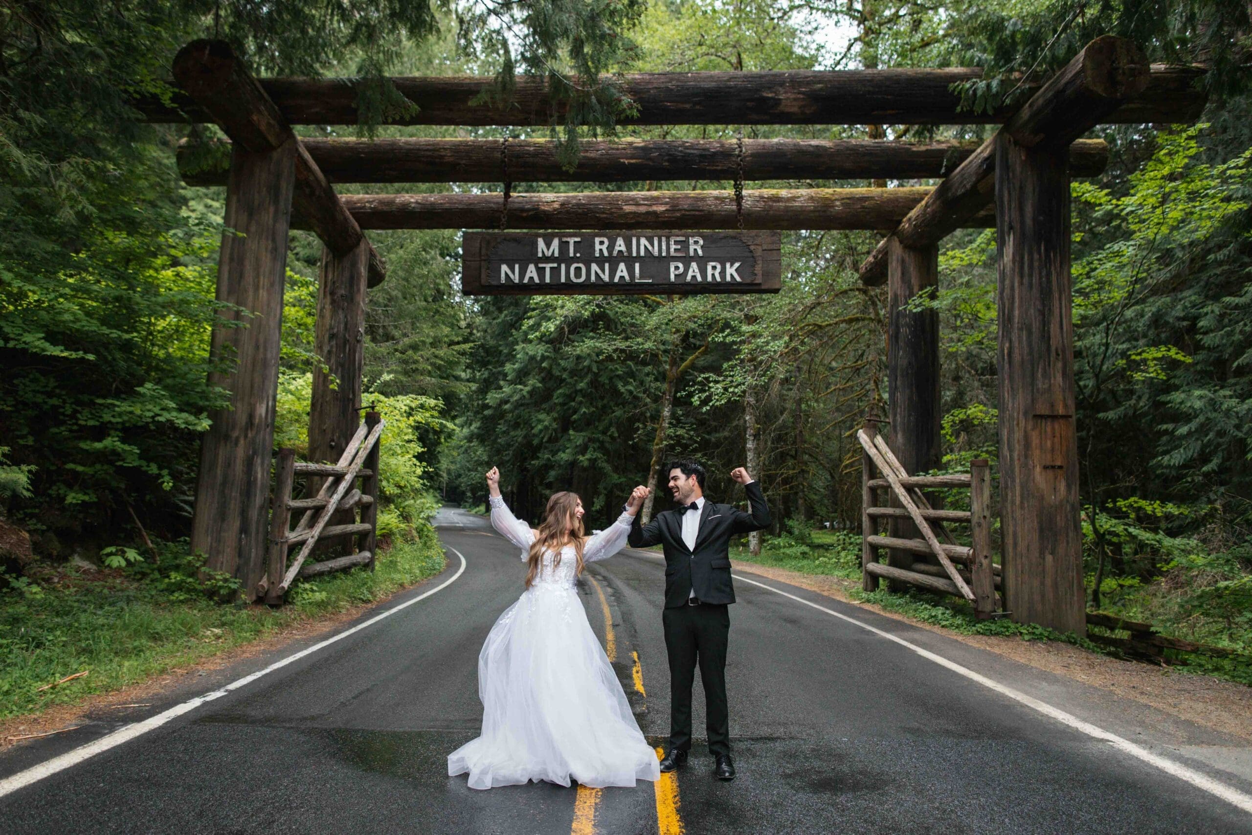 elopement couple cheers in front of the mount rainier national park sign in paradise washington